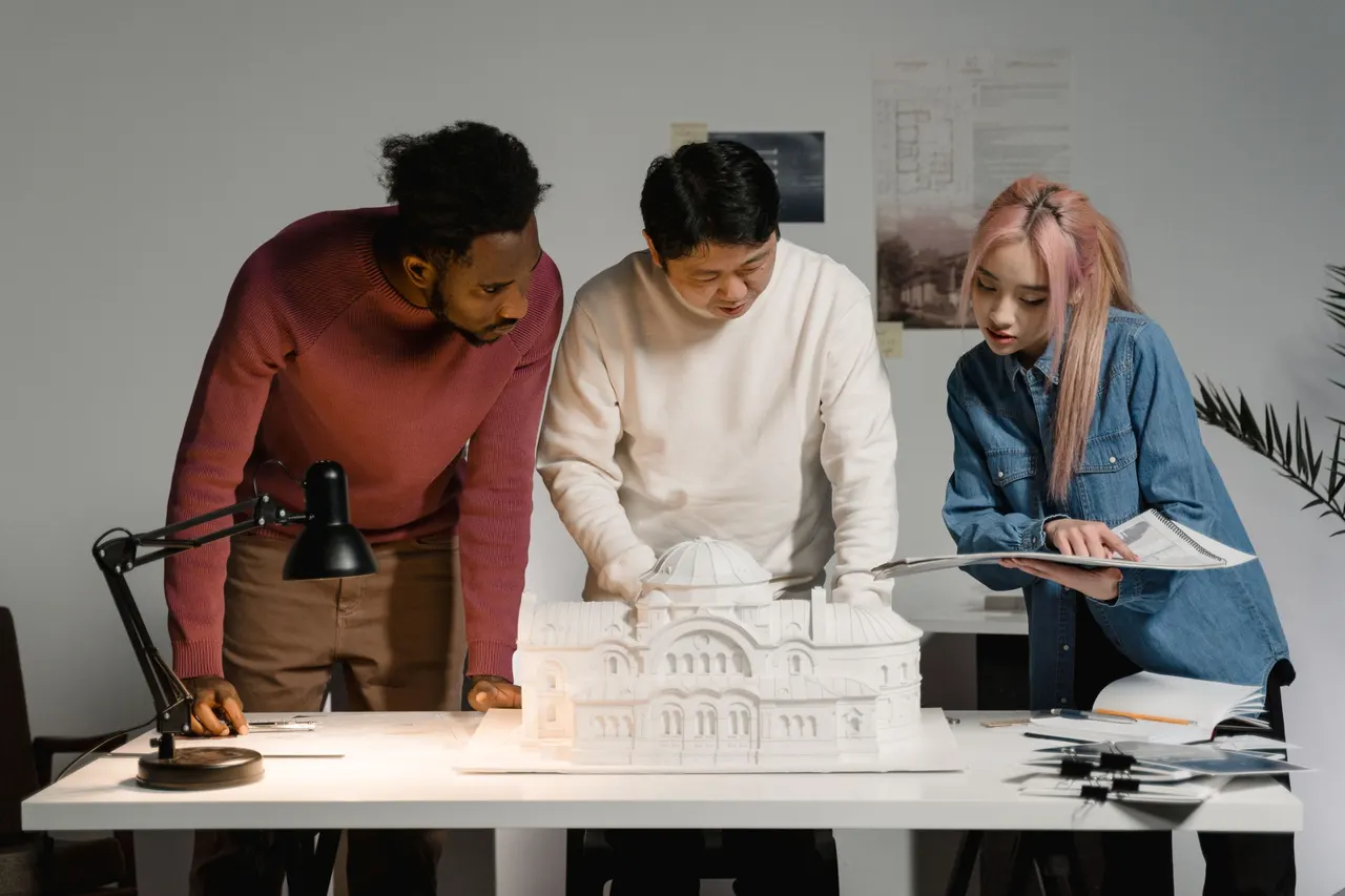 Three people studying an architectural model and drawings on a desk