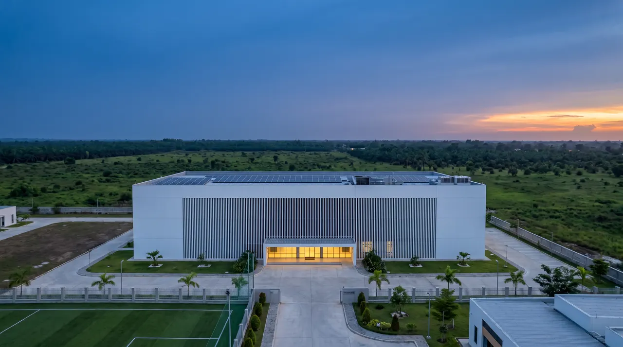 Concept of a white data centre with a finned façade and solar roof at dusk, surrounded by bush and oil palms