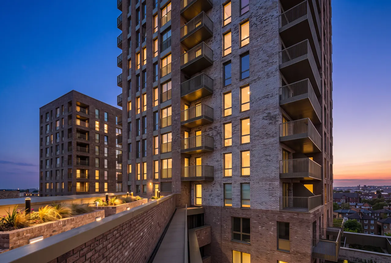 A completed Bricks‘N’Mortar residential tower in London at dusk, with balconies and a planted roof terrace