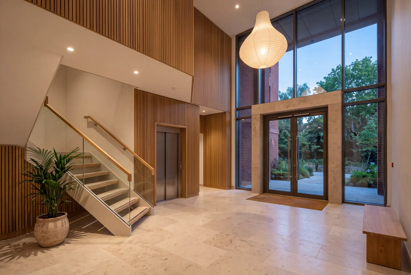 Illustration of a double-height communal entrance hall with a glass-balustrade staircase, an oak handrail and a lift