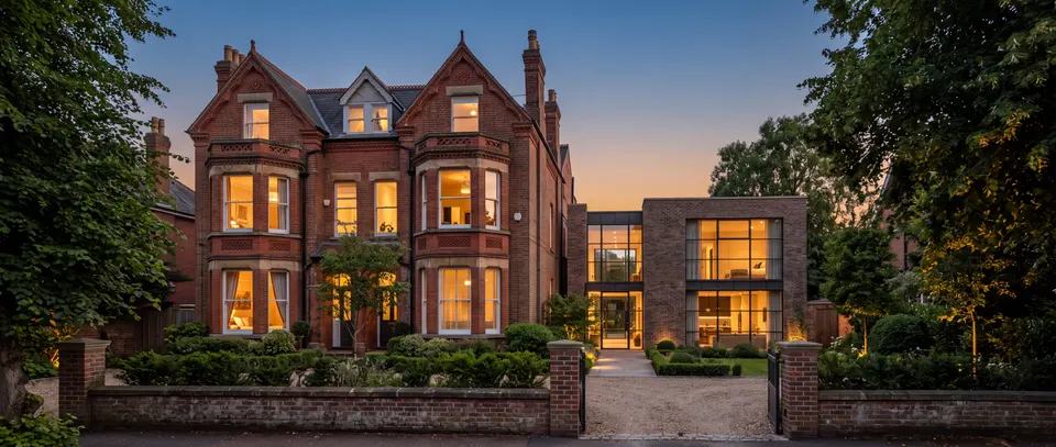 A large Victorian red-brick villa converted into flats, with a brick and glass extension and warm lit windows at dusk