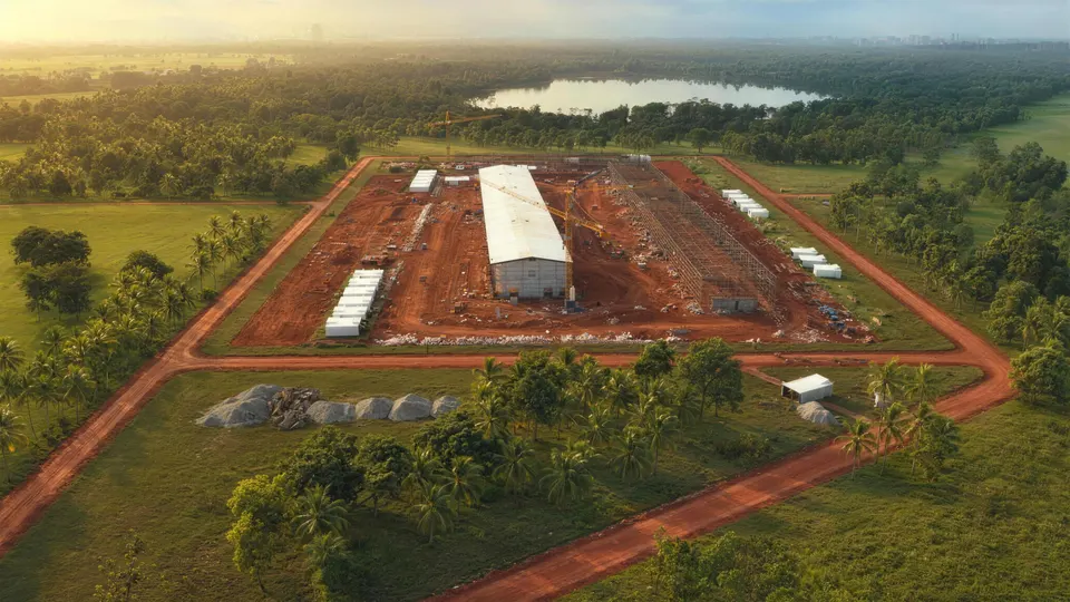 Aerial view of a development site in progress on open grassland, steel halls rising